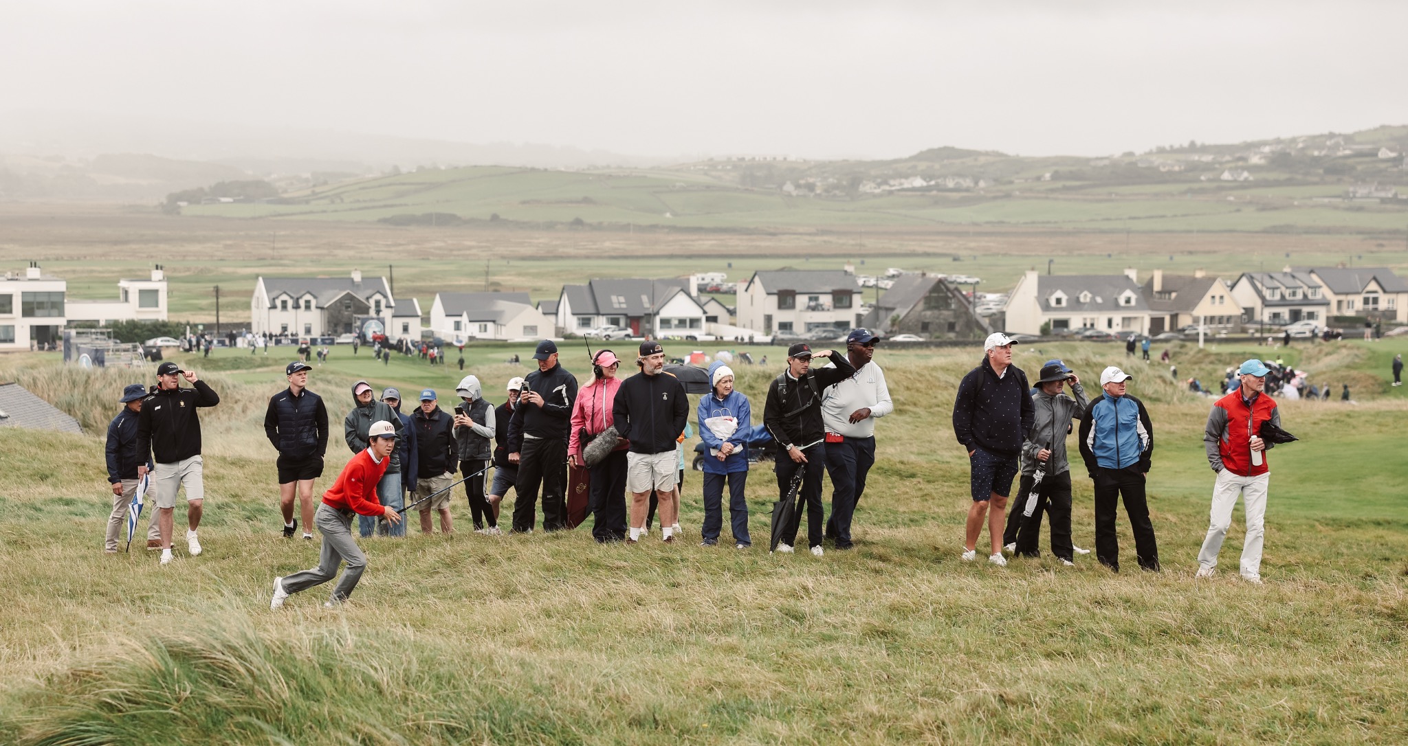 Jay Leng playing a shot from links rough as spectators watch